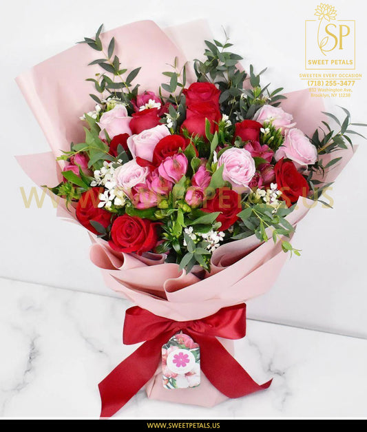 Romantic bouquet of red and blush pink roses with greenery, wrapped in soft pink paper and tied with a red ribbon, perfect for Valentine’s Day flowers.