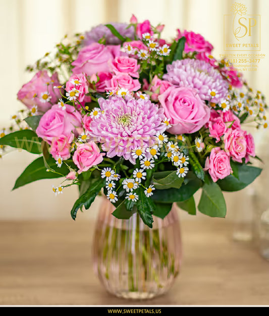 Bouquet of pink and purple flowers in a clear vase on a wooden surface with a blurred background.