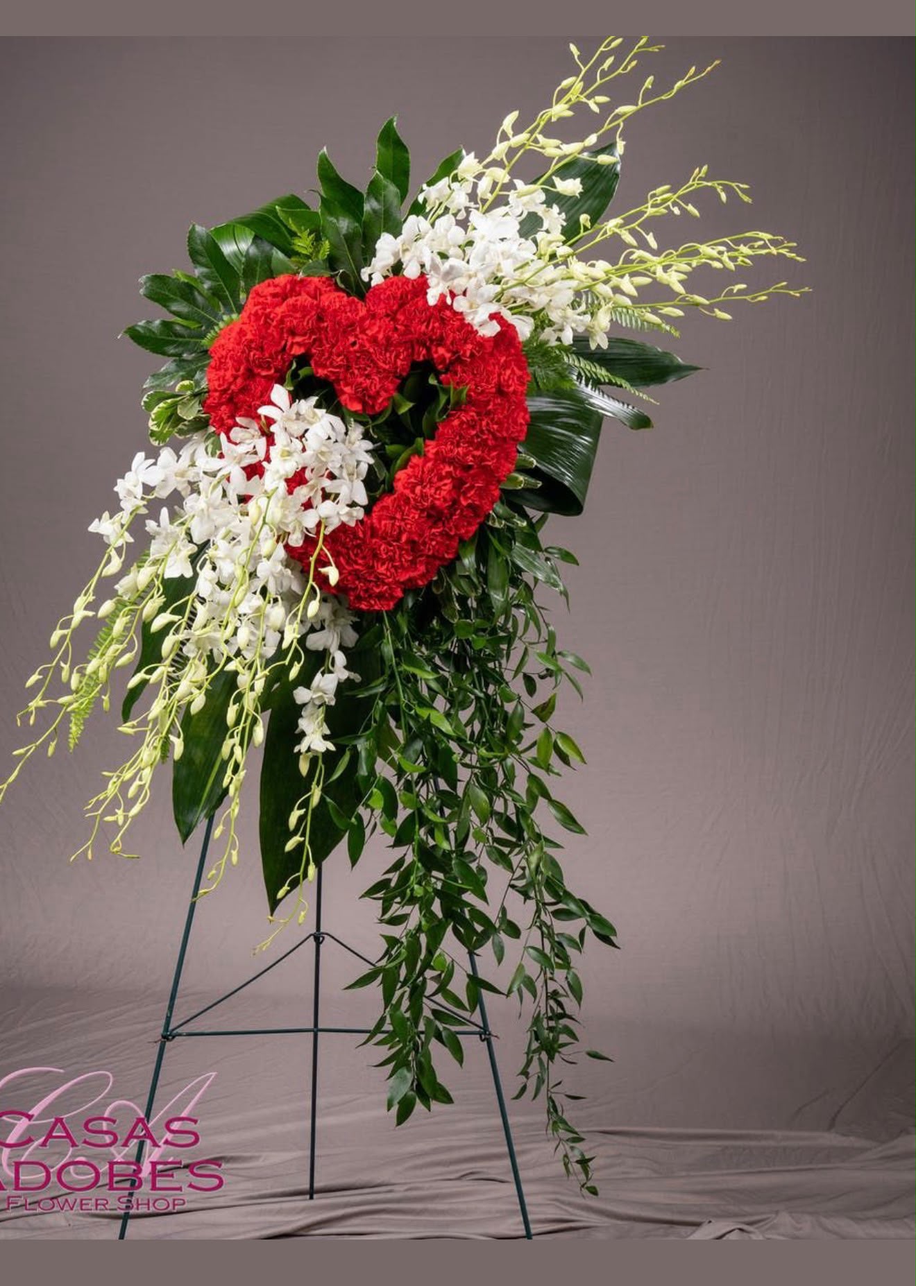 Eternal love heart sympathy standing tribute with red carnation heart wreath cascading white dendrobium orchids green cymbidium orchids and trailing greenery on standing easel – SweetPetals luxury funeral heart tribute