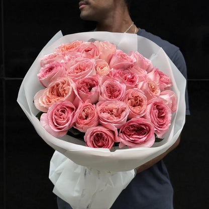 Pink garden rose luxury bouquet with deeply ruffled cupped pink and peachy-pink garden rose blooms wrapped in white tissue paper held by man in dark background – SweetPetals luxury pink garden rose birthday gift