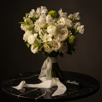 Close-up of white ranunculus white roses white sweet peas and green viburnum snowballs in garden bridal bouquet on dark marble – SweetPetals willow garden luxury wedding bouquet