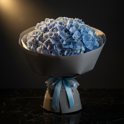 Close-up of blue hydrangea clusters in grey paper wrap with light blue ribbon on dark marble – SweetPetals serene luxury hydrangea bouquet