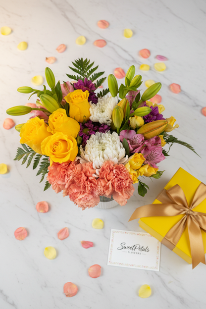 Flat lay colorful mixed flower vase with yellow gift box on marble – SweetPetals vibrant flower gift delivery