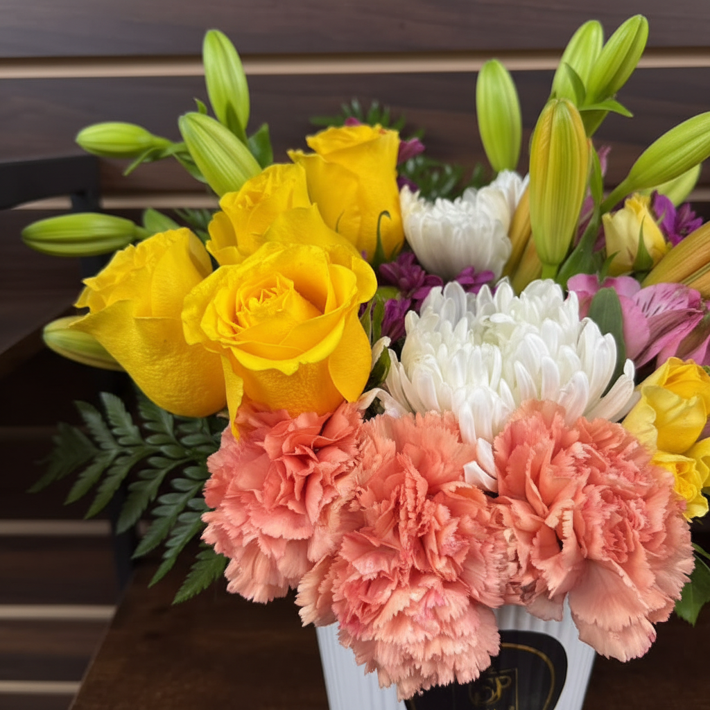 Close-up of salmon carnations yellow roses white chrysanthemums and orange lilies in white ceramic vase – SweetPetals colorful flower arrangement