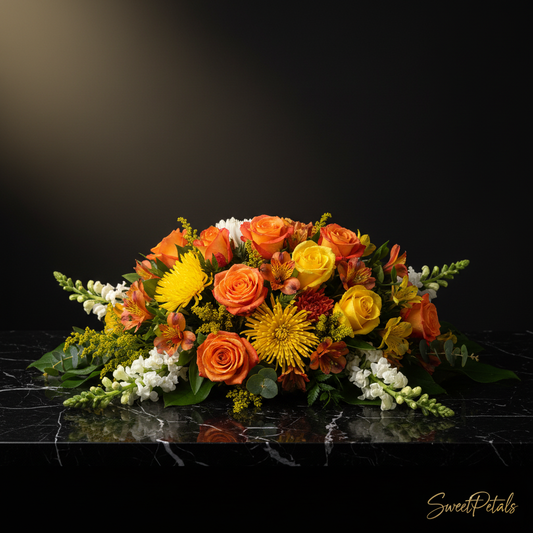 Close-up of orange roses yellow roses orange alstroemeria yellow spider mums and white snapdragons in sympathy spray on dark marble – SweetPetals golden sunrise luxury funeral flower arrangement